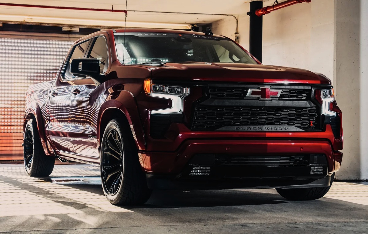 Chevrolet Silverado vermelha escura vista de frente em uma garagem, com rodas pretas e grade personalizada.