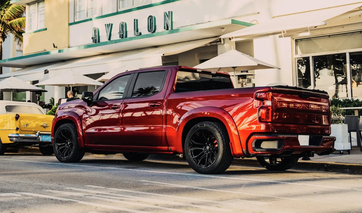 Chevrolet Silverado vermelha escura estacionada em uma rua, vista de traseira e lateral, com rodas pretas.
