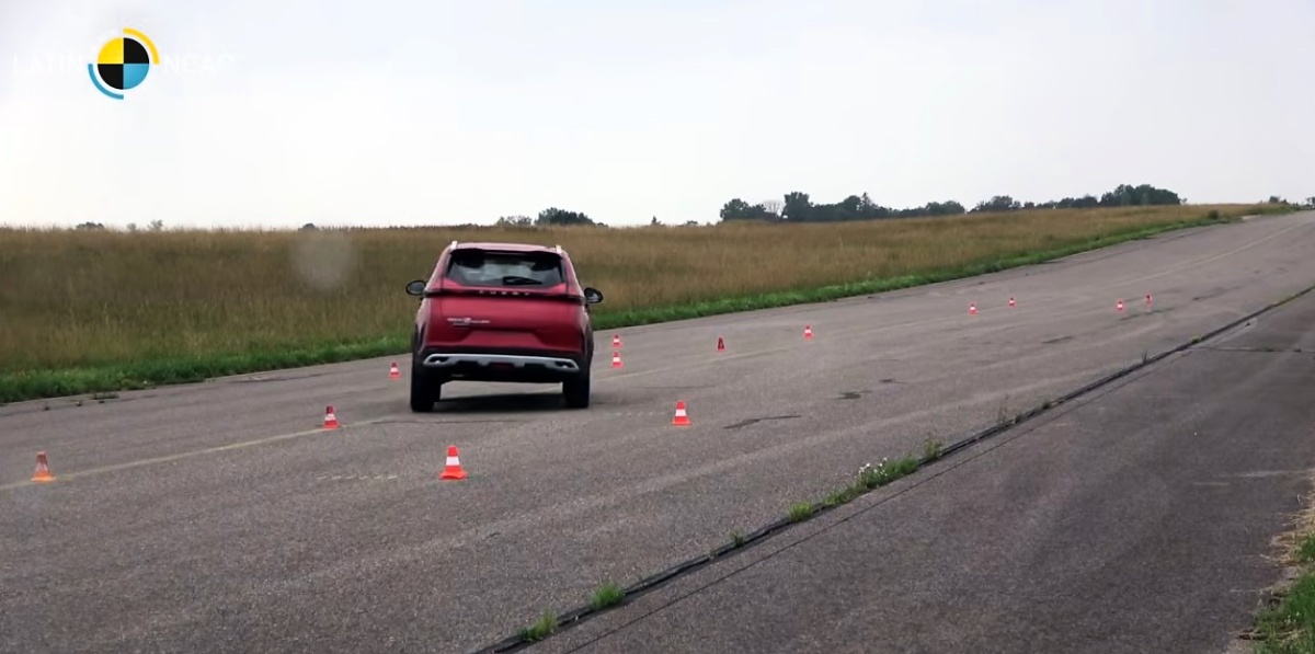 SUV vermelho visto de traseira em pista asfaltada, entre cones de sinalização.