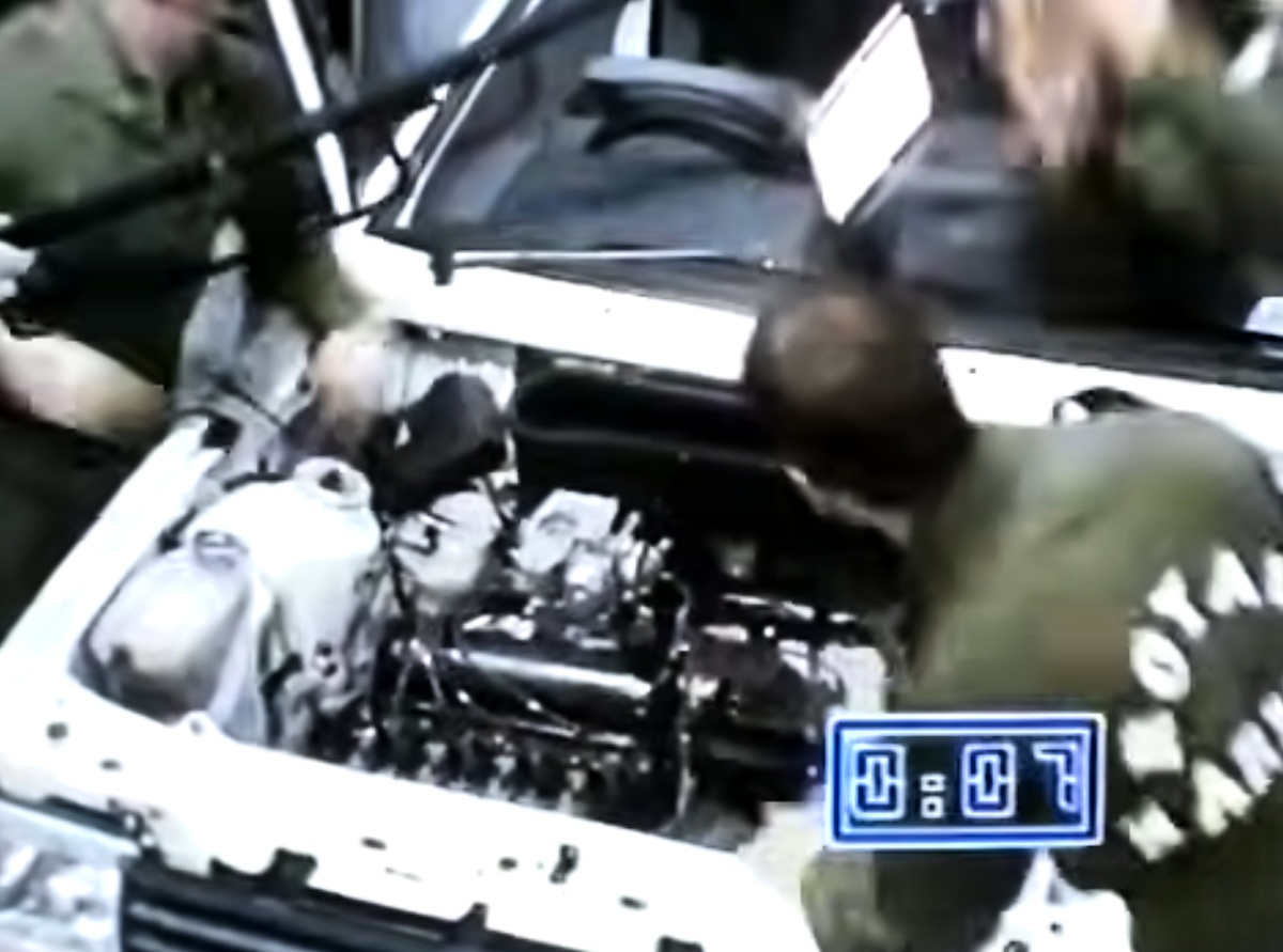 Pessoas trabalham no compartimento aberto de um carro branco; um cronômetro azul na tela marca 0:07.