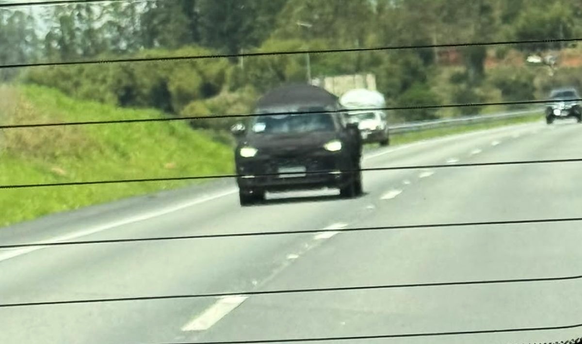Picape Volkswagen Tukan preta e camuflada vista de frente através de um vidro com linhas horizontais.