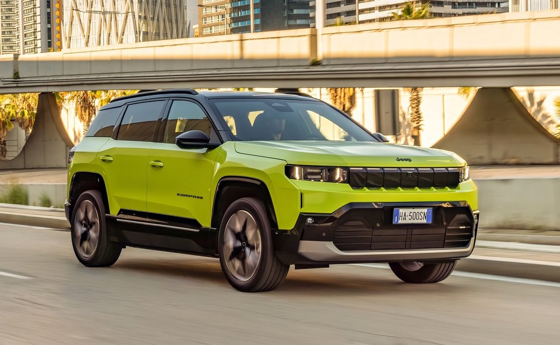 Jeep Compass verde circula em uma via urbana sob um viaduto.